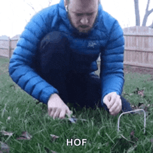 a man in a blue jacket is kneeling down in the grass and holding a wire in his hand .