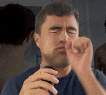 a man in a blue shirt shaving his face with a razor