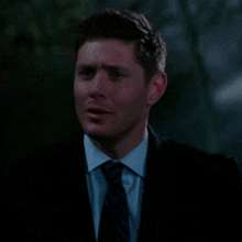 a man in a suit and tie is smiling in a dark room