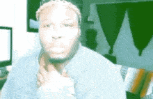 a man in a gray sweater is sitting in a living room with his hand on his chin .