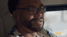 a man with glasses and a beard is sitting in a car and smiling .
