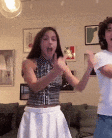 a woman in a plaid top and white skirt is dancing in a living room