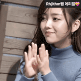 a woman in a blue turtleneck is clapping her hands with rhythm written on the bottom right