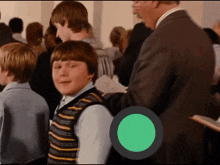 a boy in a striped vest stands in a crowd with a green circle in the middle