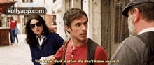 a man in a red shirt is talking to a man in a hat and a woman in a blue jacket .