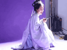 a woman in a white dress is holding a sword in front of an aputure machine