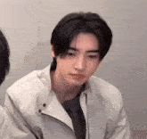 a young man with black hair is wearing a white jacket and a black shirt .
