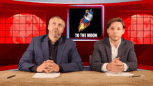 two men sit at a desk in front of a screen that says to the moon