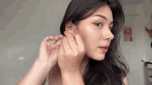 a woman is putting on a pair of earrings in her left ear .