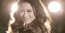 a woman with long hair is smiling in front of a bright light .
