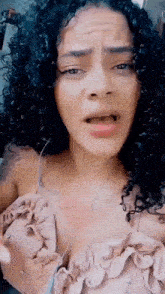 a woman with curly hair is making a funny face while wearing a ruffled top .
