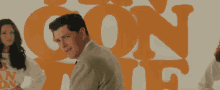 a man in a suit and tie stands in front of a wall with the word con on it