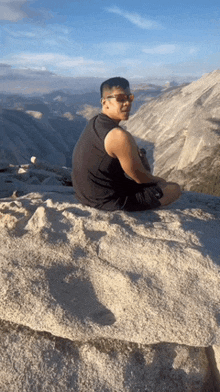 a man wearing sunglasses is sitting on top of a rocky mountain