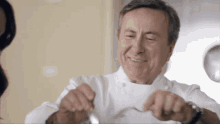a man in a chef 's uniform is smiling while holding a spoon and fork