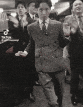 a black and white photo of a group of men in suits and ties dancing .