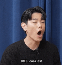 a man in a black sweater says omg cookies in front of a blue curtain
