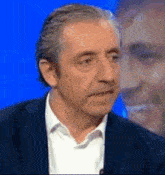 a man in a suit and white shirt is talking on a microphone on a blue screen .
