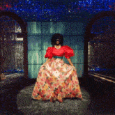 a woman wearing a red top and floral skirt