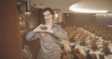 a man making a heart shape with his hands in front of rows of chairs