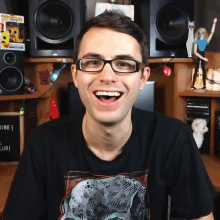 a man wearing glasses and a black shirt with a dinosaur on it smiles
