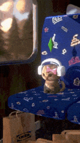 a pug wearing headphones sits on a blue seat next to an ikea shopping bag