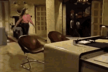 a woman in a pink shirt is walking through a room with chairs and a desk