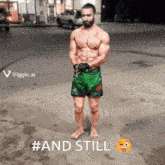 a shirtless man in green shorts is standing on a street with the words #and still written below him