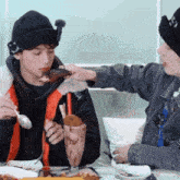 two young men are sitting at a table eating food and drinking a milkshake