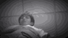 a black and white photo of a man laying on a bed with his hands on his chest .