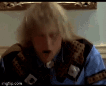 a man with blonde hair is wearing a blue shirt and a brown jacket