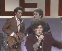 a man playing a guitar and singing into a microphone in front of a sign that says let