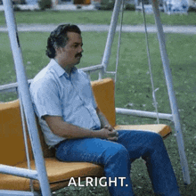 a man with a mustache is sitting on a swing and says `` alright '' .