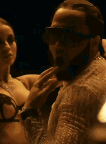 a man wearing sunglasses is standing next to a woman in a bra .