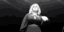 a black and white photo of a woman standing on a stage in a dark room .