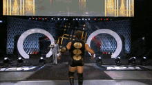 a wrestler in a black and gold outfit walks down the aisle of a wrestling arena
