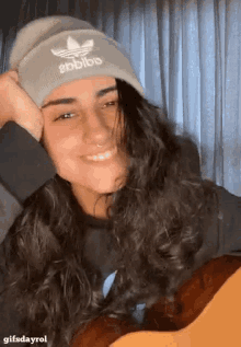 a woman wearing an adidas beanie is smiling and holding a guitar .