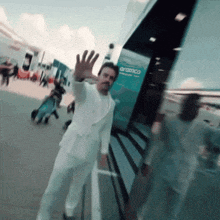 a man in a white suit is waving in front of a building that says aramco