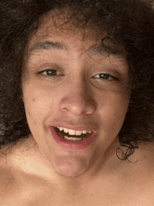 a shirtless man with curly hair is smiling and making a funny face