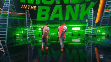 two men are standing on a stage in front of a green sign that says ' in the bank ' .