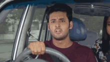 a man in a maroon shirt is driving a car with a woman in the back seat