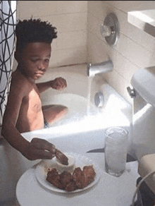 a young boy is taking a bath in a tub while eating chicken wings .