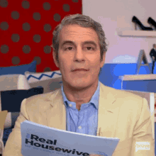 a man in a suit and blue shirt is holding a piece of paper that says `` real housewife '' .