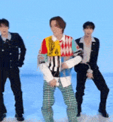 a man in a colorful sweater and plaid pants is dancing with two other men on a blue background .