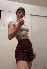 a woman wearing a crop top and plaid shorts is standing in front of a wall .