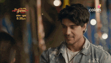 a man in a denim jacket is smiling in front of an ad for colors