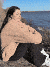 a woman is sitting on a rock by the water