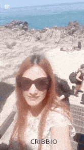 a woman wearing sunglasses takes a selfie with the word cribbio in the lower right corner