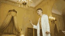 a man in a white robe is standing in a room with a chandelier