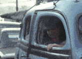 a man in a hat looks out the window of a blue car