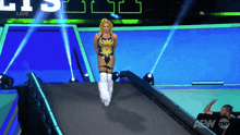 a woman in a wrestling outfit walks down a ramp with a aew tv logo behind her